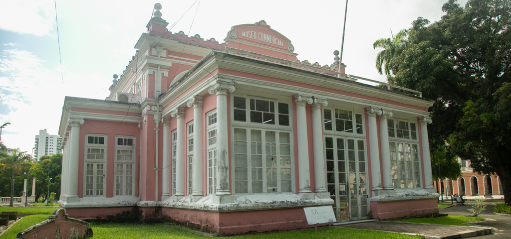 Fotografia da fachada do Instituto de Ciências da Arte da UFPA. É um prédio histórico nas cores branca e rosa. Ao redor, há gramados.