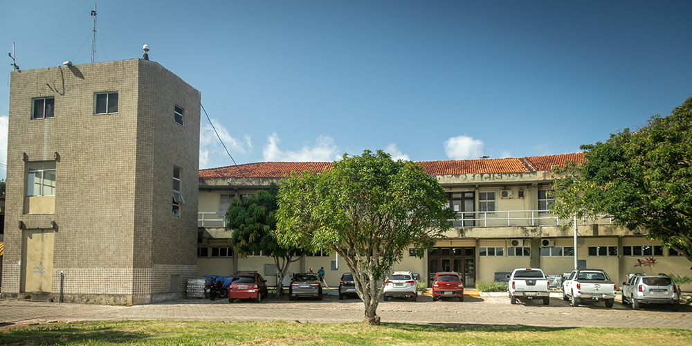 Fotografia da fachada do Instituto de Geociências da UFPA. Em frente, há uma árvore e carros estacionados.