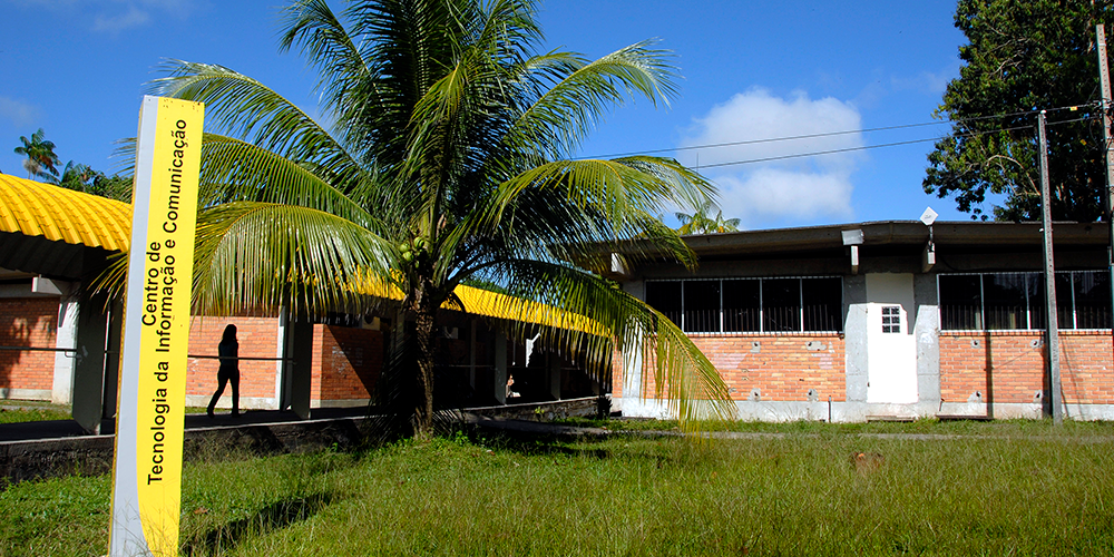 Fotografia da fachada do Centro de Tecnologia da Informação e Comunicação da UFPA. Em frente ao prédio, há uma grande palmeira e uma passarela coberta.
