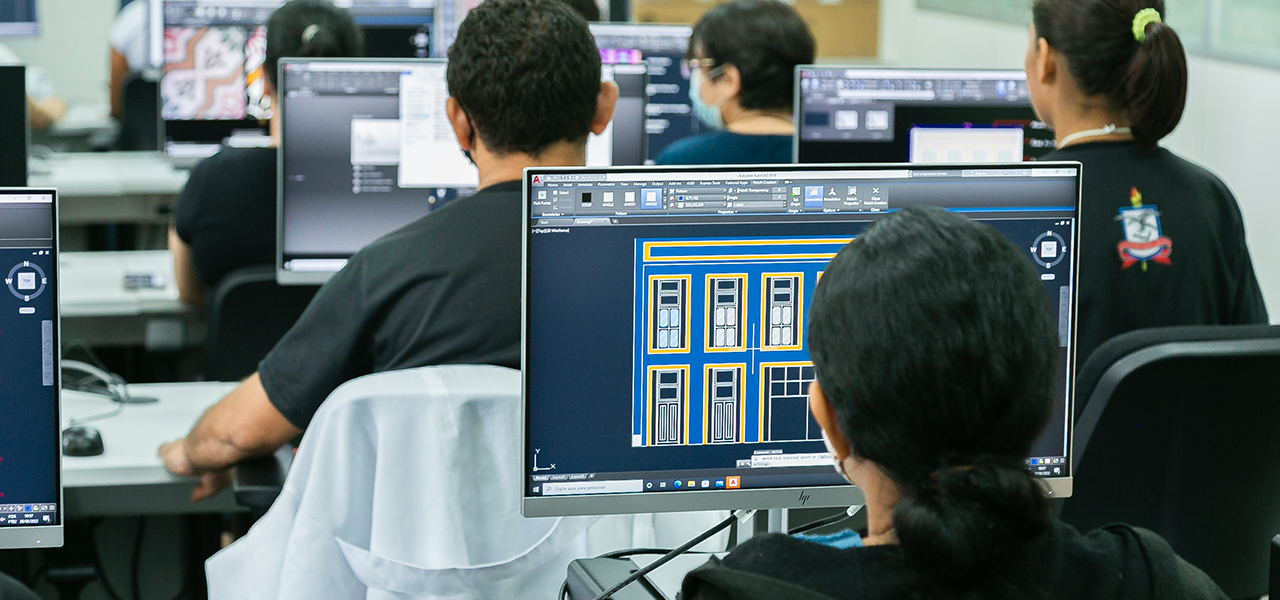 Fotografia de estudantes sentados em frente a computadores em um laboratório de informática.
