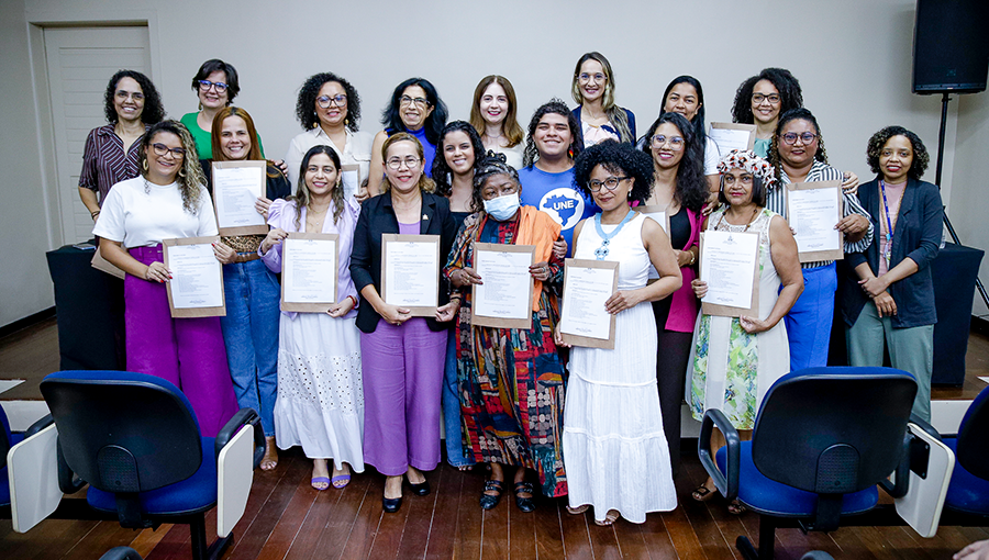 Fotografia posada com grupo de mulheres que compõe a Comissão para Equidade de Gênero na UFPA. Várias delas seguram um documento nas mãos.