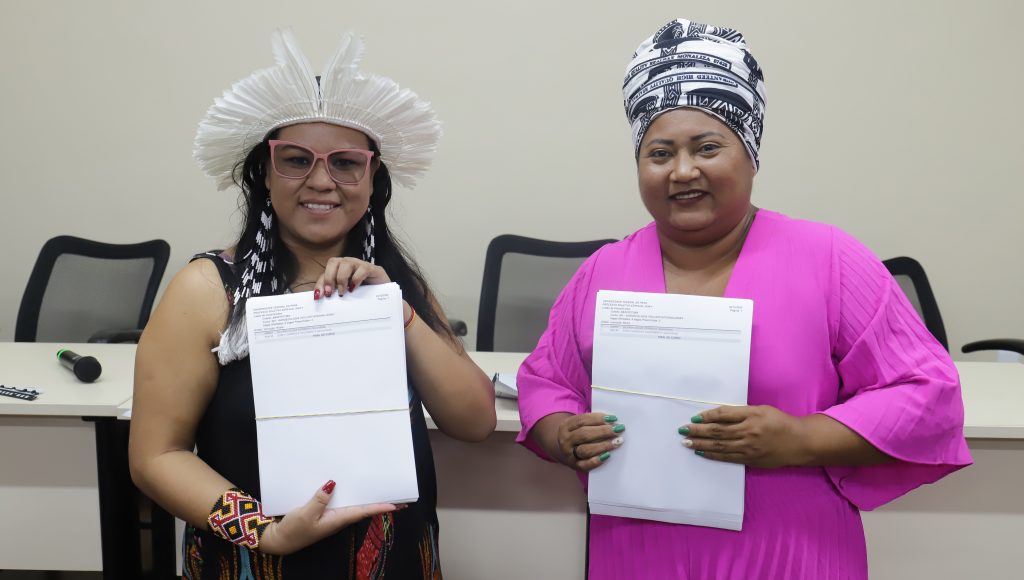 Fotografia posada das representantes da Associação dos Povos Indígenas Estudantes (APYEUFPA), Josilene Nunes; e da Associação dos Discentes Quilombolas (ADQ); Vanuza Cardoso. Elas seguram o listão com os nomes dos aprovados no PSE Indígenas e Quilombolas 2024.