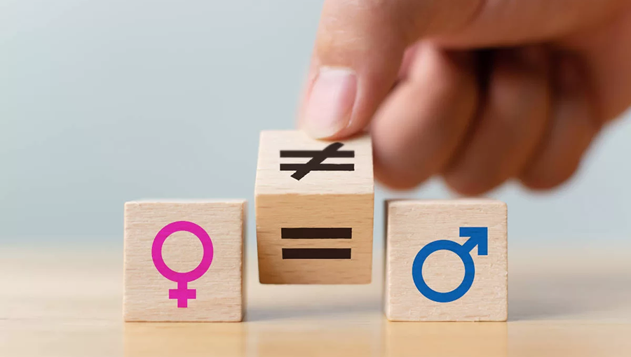 Fotografia de três cubos. No primeiro, à esquerda, está o símbolo de feminino. No do meio, está o símbolo matemático de igualdade. E no terceiro, à direita, está o símbolo de masculino. Aparece o pedaço de uma mão segurando o cubo do meio.