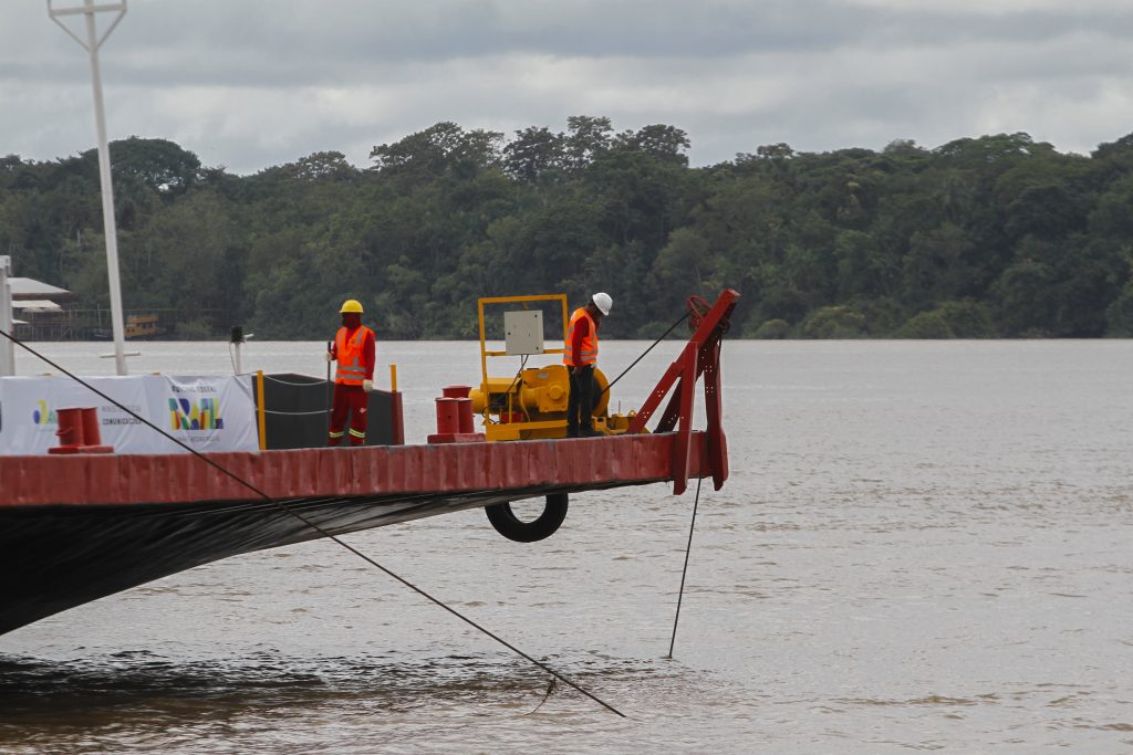 Fotografia destaca parte da estrutura da plataforma ancorada no rio Guamá. A imagem destaca dois operários sobre a plataforma e dois cabos que ligam a estrutura às águas. 