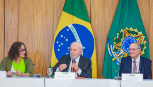 Fotografia do presidente lula falando em uma bancada. À sua esquerda está a ministra de Ciência e Tecnologia Luciana Santos e, à sua direita, está o vice-presidente Geraldo Alckmin.