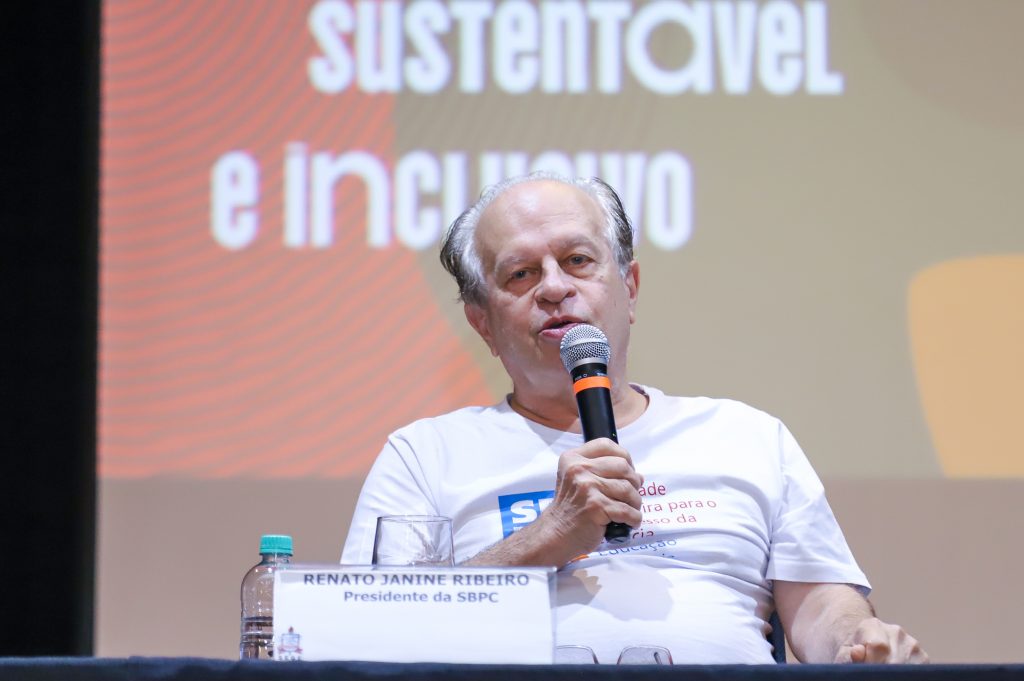 Fotografia do presidente da SBPC, Renato Janine. Homem branco, de cabelos grisalhos. Ele usa camiseta branca, está sentado e fala ao microfone. 