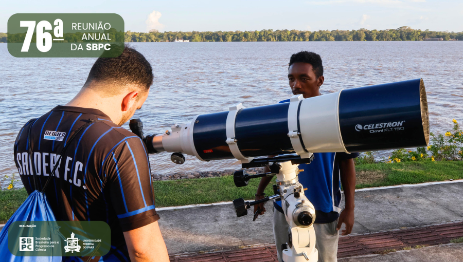 Fotografia de dois homens na beira do rio. Um deles olha por um telescópio, ele está de costas para a foto, o outro o observa. Comissão Local de Comunicação da 76ª da Reunião Anual da SBPC