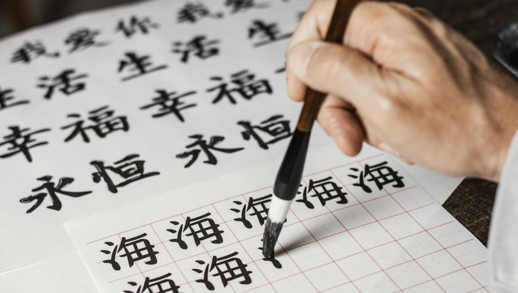 Fotografia de um ângulo alto registra uma mão escrevendo símbolos chineses em papelbranco
