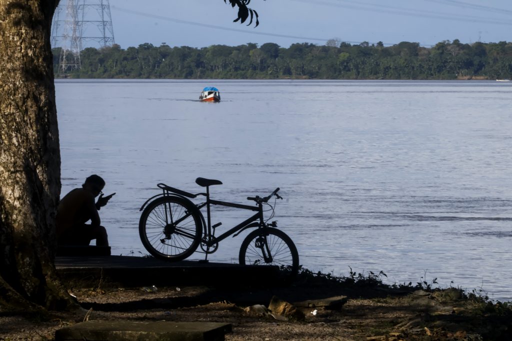 Fotografia da orla da UFPA. Em destaque, a silhueta de uma pessoa sentada na orla do rio.
