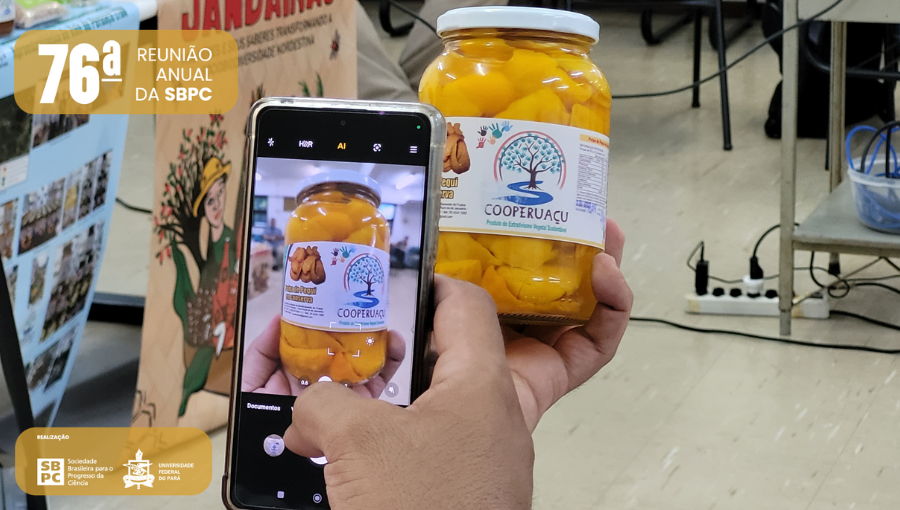 Fotografia registra a tela de um celular, que está focando em um pote de compota de um fruto amarelo. Na parte superior da imagem, à esquerda, o logo da SBPC. Na parte inferior, à esquerda, o logo da SBPC e o brasão da UFPA.