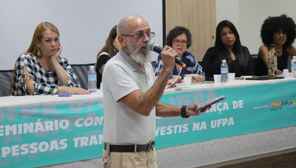 Raicarlos Coelho Durans fala ao microfone enquanto é observado pelas integrantes de uma das mesas realizadas no evento.
