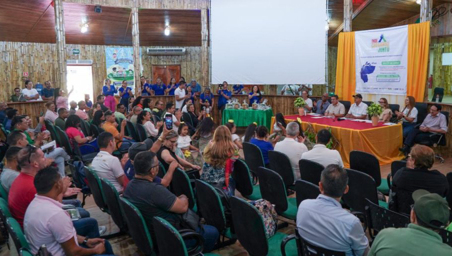 Fotografia de um auditório lotado. No canto superior direito, em destaque, a mesa do evento formada por sete pessoas, sendo três mulheres e quatro homens.