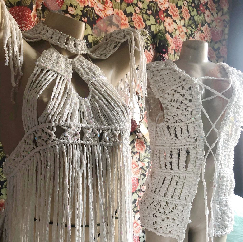 Fotografia registra dois manequins vestidos com criações feitas com sacolas de plástico. As peças tem cor clara, próxima ao branco.