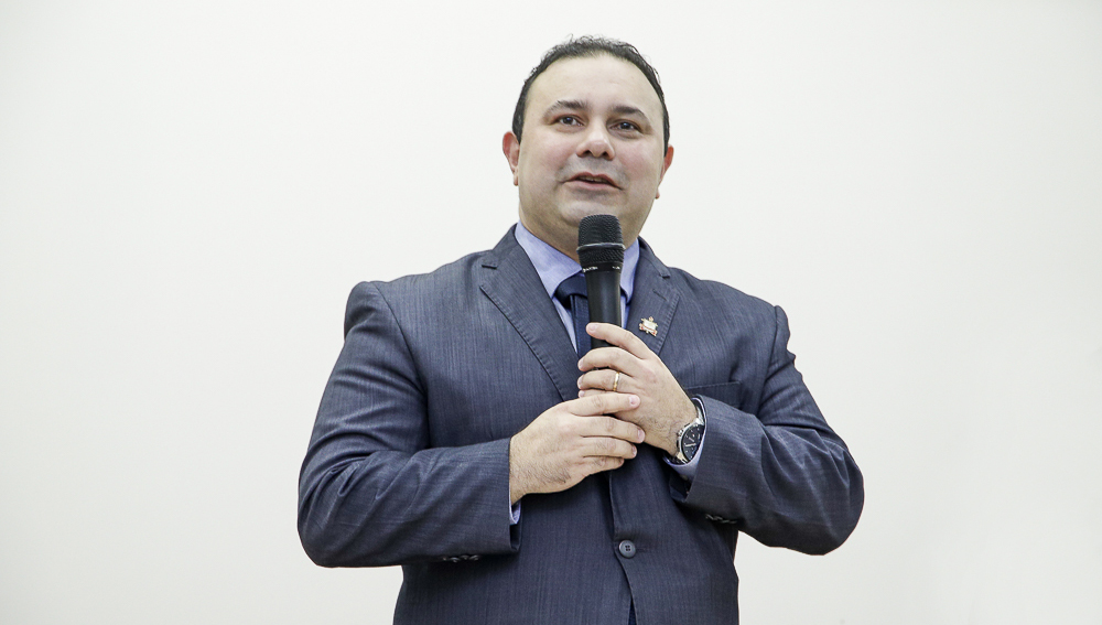 Fotografia do novo diretor-adjunto do ICB, professor Luís Adriano. Ele é um homem branco, tem cabelos pretos curtos, veste roupa social e fala ao microfone.