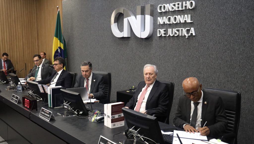Fotografia registra o reitor da UFPA, Gilmar Pereira da Silva, assinando um documento enquanto é observado pelo Ministro da Justiçã, Ricardo Lewandowski, e pelo presidente do Supremo Tribunal Federal (STF), Luís Roberto Barroso.