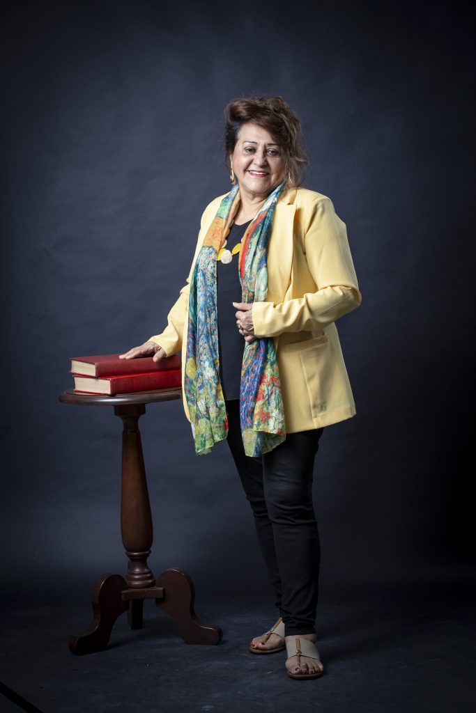 Mulher em pé apoia as mãos sob dois livros que estão em cima uma mesa redonda de madeira.