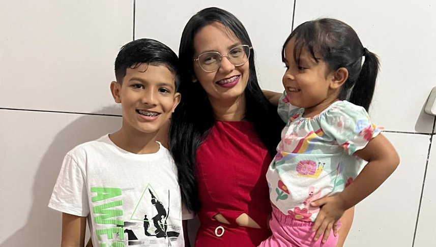 Fotografia posada de Bianca, mulher parda de cabelos pretos, longos e liso, com duas crianças: um menino e uma menina, que está em seu colo.