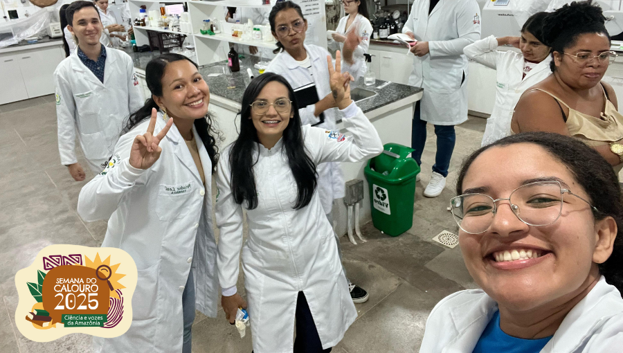 Fotografia posada e descontraída de um grupo de pessoas. Eles estão em um laboratório, veste jaleco branco e sorriem pra foto.
