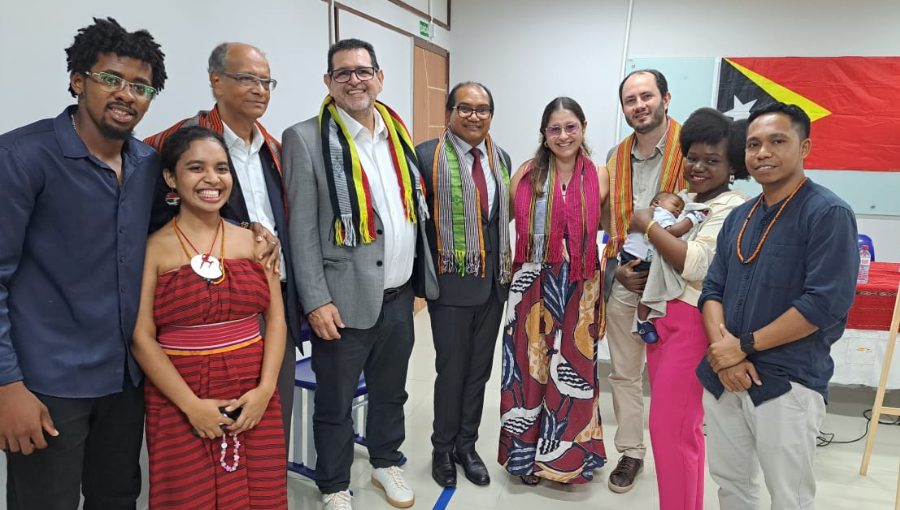 Fotografia posada de um grupo de pessoas. Ao fundo, é possível idenitifcar uma bandeira do Timor Leste pendurada na parede.