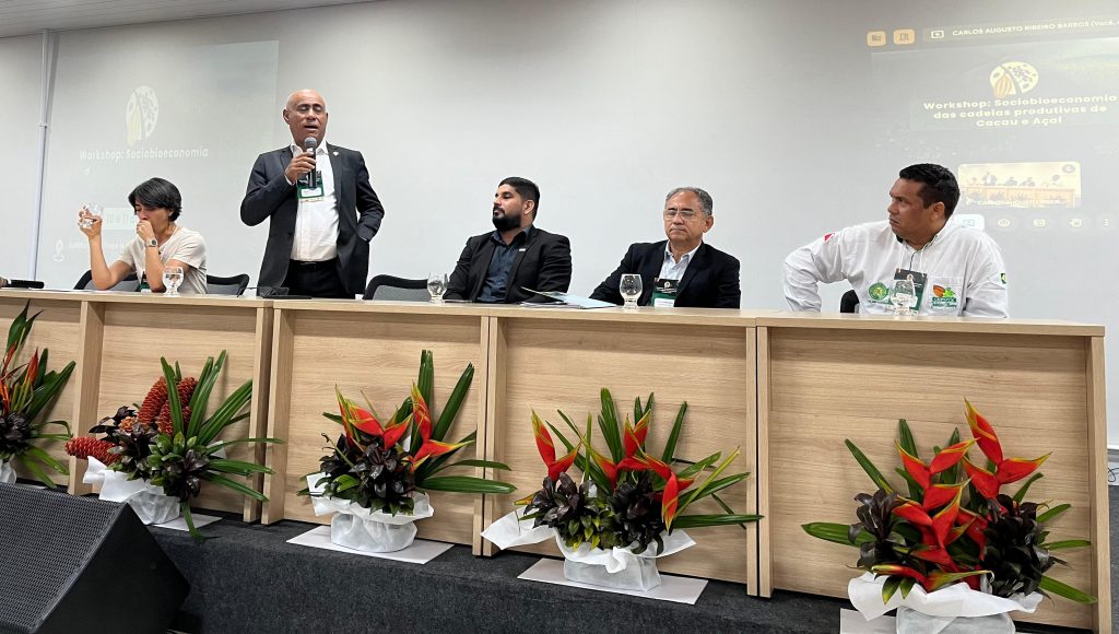 Fotografia da mesa de um evento, entre as pessoas está o reitor da UFPA, Gilmar Pereira da Silva, que está em pé e fala ao microfone.