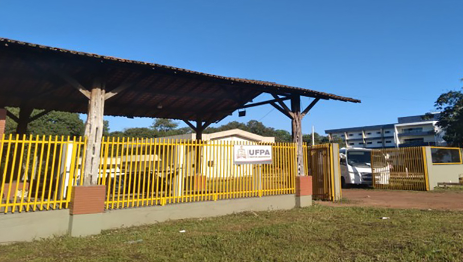 Fotografia da entrada de um prédio. É possível identifica muro com grades. Na grade há uma placa com a seguinte identificação: UFPA Campus Ananindeua.