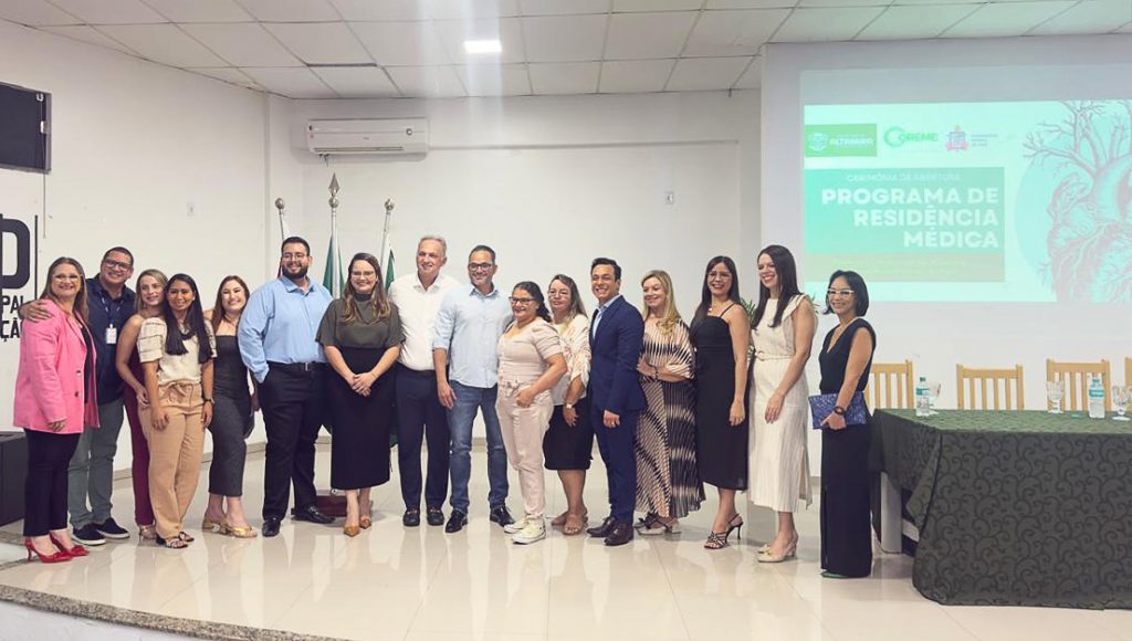 Fotografia posada de um grupo de pessoas. Eles estão disposto em frente a um tela, onde está projetado o seguinte texto: PROGRAMA DE RESIDÊNCIA MÉDICA.