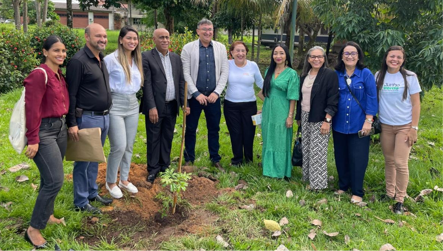 Fotografai posada de um grupo de pessoas, eles estão próximos de uma muda de planta.