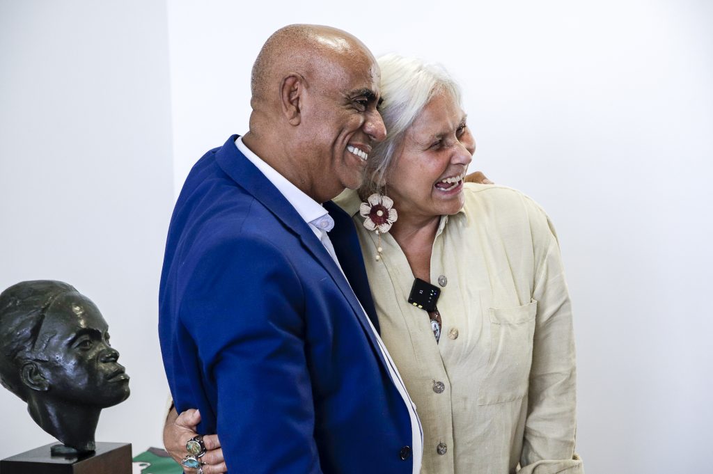 Fotografia registra o reitor da UFPA Gilmar Pereira da Silva e a cantora Fafá de Belém em momento de descontração. Os dois estão abraçados e sorriem,
