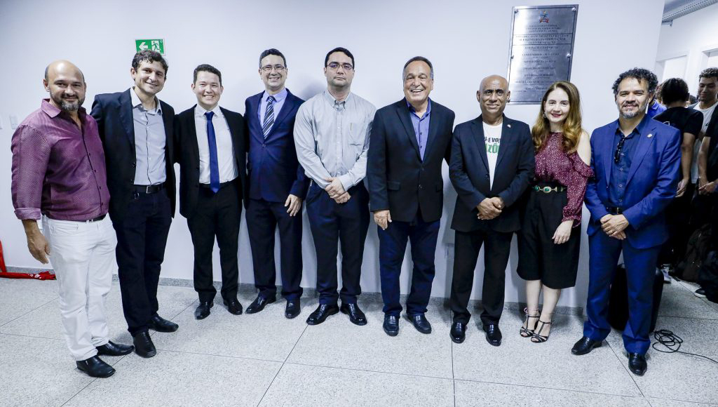 Fotografia posada de um grupo de pessoas que se colocaram a frente de uma placa.