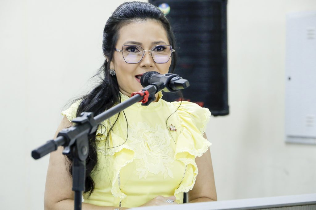 Fotografia da vice-coordenadora do campus, Raquel Furtado. Ela é uma mulher de pele clara, cabelos longos de cor preta. Ela usa roupa de cor amarela e fala ao microfone.