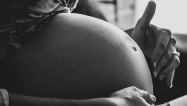 Fotografia preto e branca registra a barriga de uma pessoa grávida.