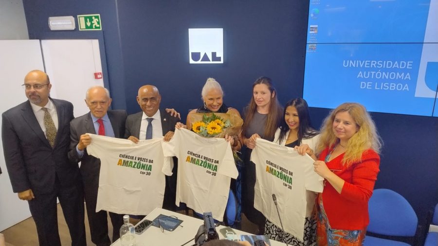 Fotografia mostra grupo de pessoas, formado por homens e mulheres. Eles estão de pé e exibem nas mãos três camisetas brancas com a inscrição: Ciência e Vozes da Amazõnia