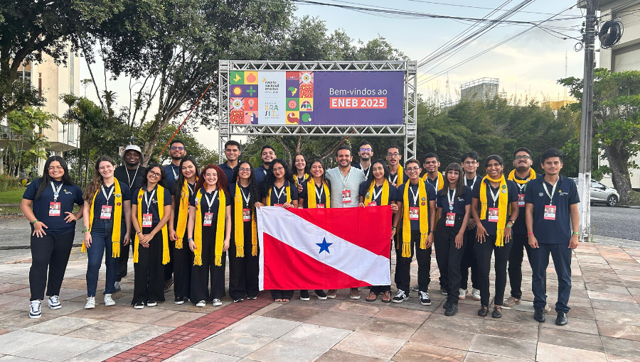 Fotografia mostra grupo de pessoas de pé e posando para a foto. O grupo segura a bandeira do estado do Pará (Vermelha com uma faixa transversal branca e uma estrela). A maioria do grupo veste roupa preta e usa uma faixa amarela em volta do pescoço.