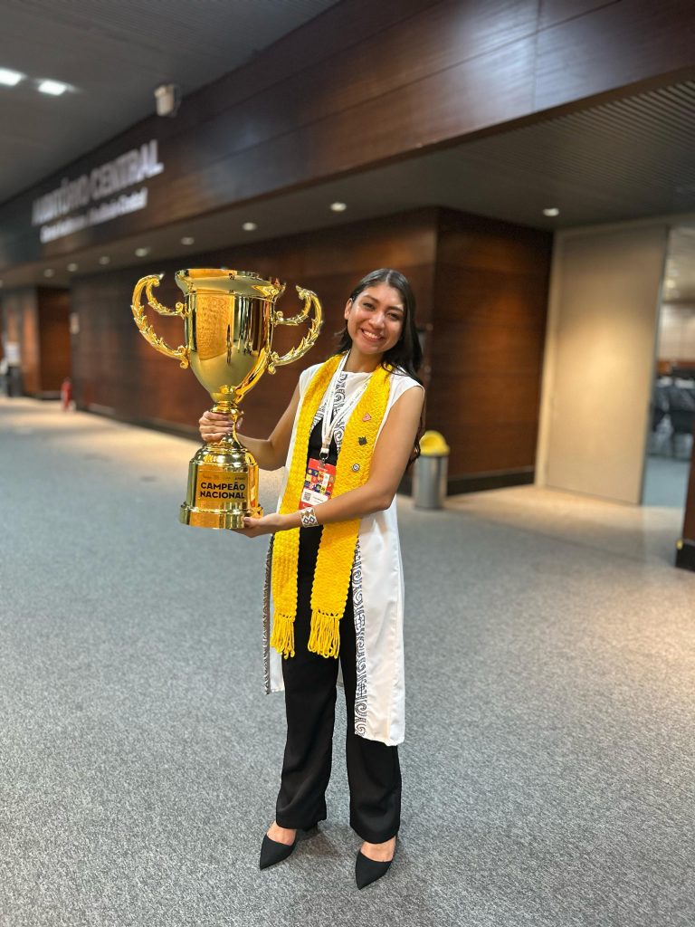 Fotografia jovem parda de pé segurando um grande troféu dourado.