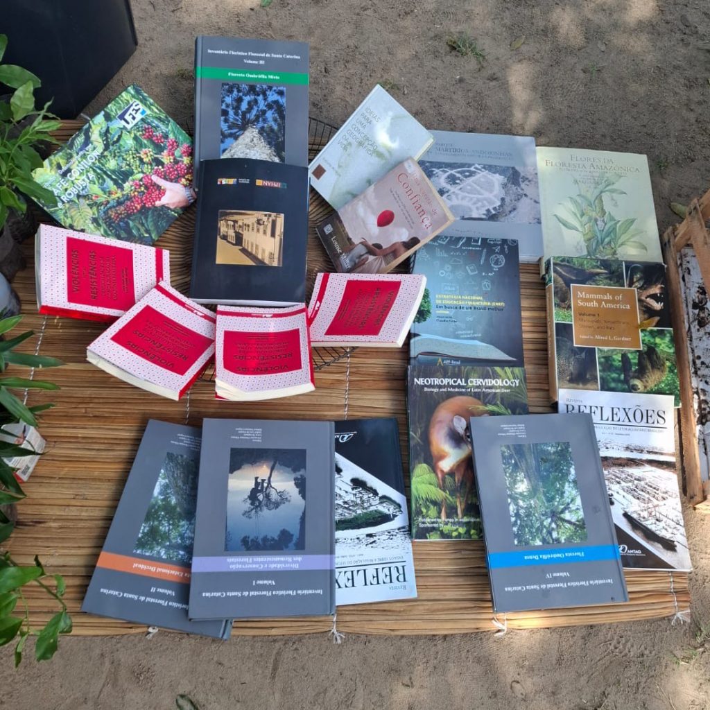 FOTOGRAFIA REGISTRA ALGUNS LIVROS DISPOSTOS SOBRE UMA ESTEIRA EM UM CHÃO DE AREIA.
