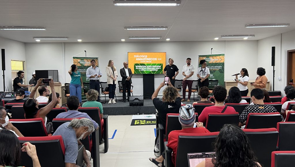 Fotografia de um auditório, com destaque para um grupo de pessoas no palco ao fundo.