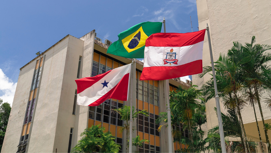Fotografia destaca três bandeiras hasteadas: do Pará, do Brasil e da da UFPA. Ao fundo, prédio da Reitoria.