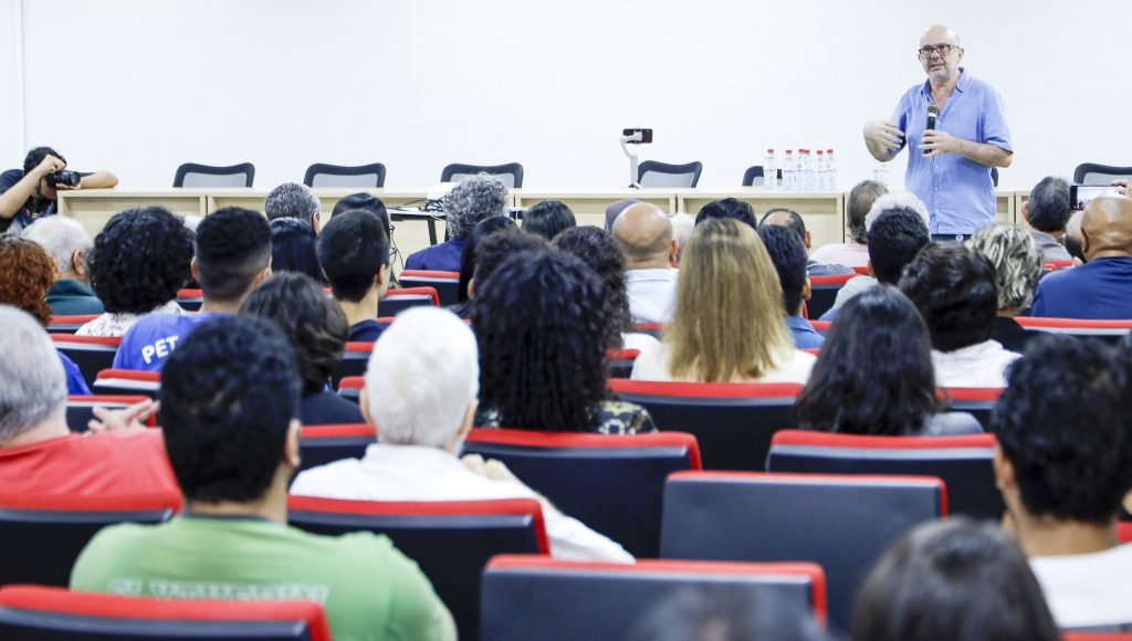 Fotografia registra, sem segundo plano, o professor Luiz Crispino falando ao microfone para uma grande plateia em um auditório.