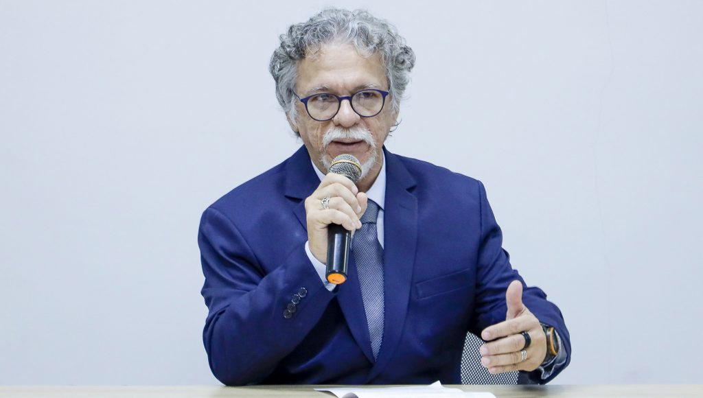 Fotografia do professor Ari Loureiro, enquanto ele fala ao microfone.