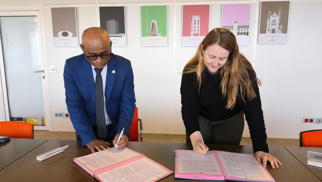 Fotografia do Reitor da UFPA, Gilmar Pereira da Silva, e da diretora da Ensa Paris-Belleville, Christine Leconte, assinando documentos dispostos em uma mesa de madeira.
