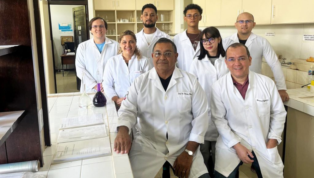 Fotografia posada de um grupo de pesquisadores. Eles estão dentro de um laboratório, vestidos com jalecos brancos.