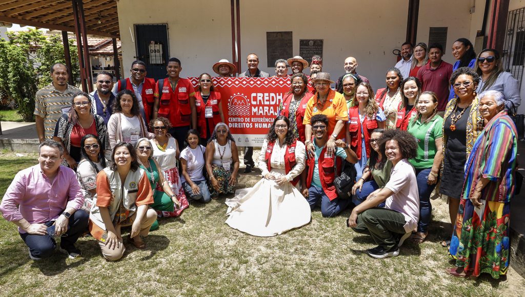 Fotografia registra um grupo de pessoas posando ao lado da placa de identifica do prédio do CENTRO DE REFERÊNCIAS EM DIREITOS HUMANOS - CREDH MARAJO. Abaixo da identificação, a logo do Governo federal, do Ministérios dos Direitos Humanos e da Cidadanioa, e o brasão da UFPA.