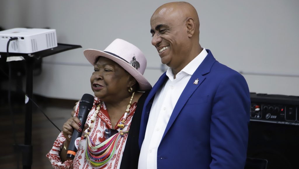 Fotografia registra a professora Zélia Amador de Deus falando ao microfone, ao lado do reitor da UFPA, Gilmar Pereira da Silva.
