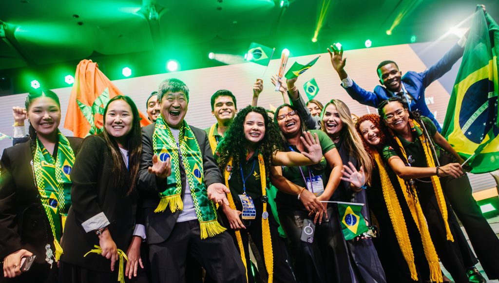 Fotografia registra um grupo de jovens, vestidos de preto com acessórios nas cores verde e amarelo, incluindo pequenas bandeiras do Brasil.