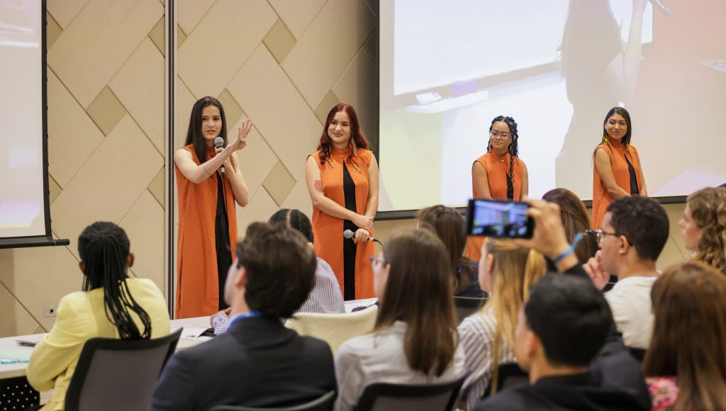 Fotografia registra quatro jovens mulheres se apresentando para uma plateia.