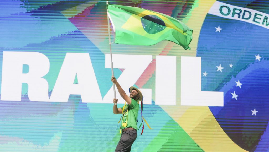Fotografia registra um jovem balançando uma grande bandeira do Brasil.