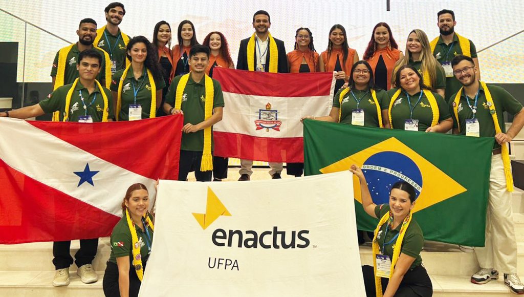 Fotografia posada de um grupo de pessoas. Eles seguram as bandeiras do Pará, da UFPA, do Brasil e da Enactus UFPA.