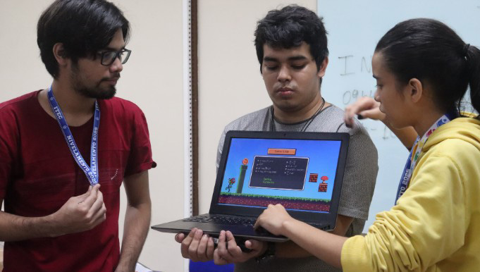 Fotografia de três jovens mostrando um aplicativo na tela de um notebook.