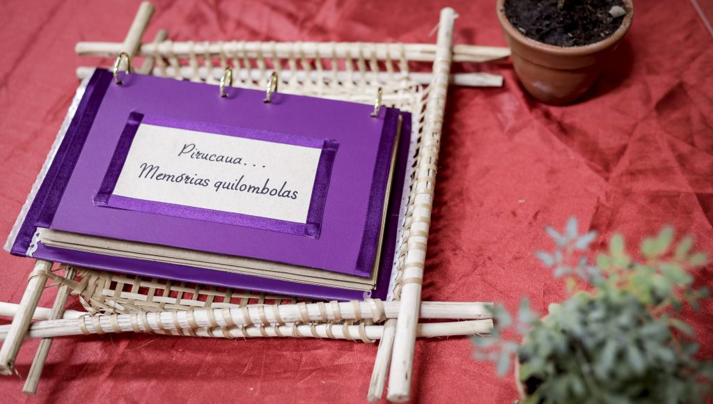 Fotografia registra um álbum com a seguinte identificação na capa: PIRUCAUA... MEMÓRIAS QUILOMBOLAS.