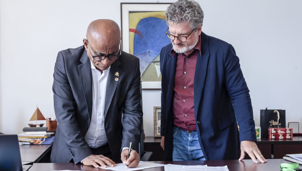 Fotografia registra o momento que o reitor da UFPA, Gilmar Pereira da Silva, assina um documento, sendo observado por um outro homem.